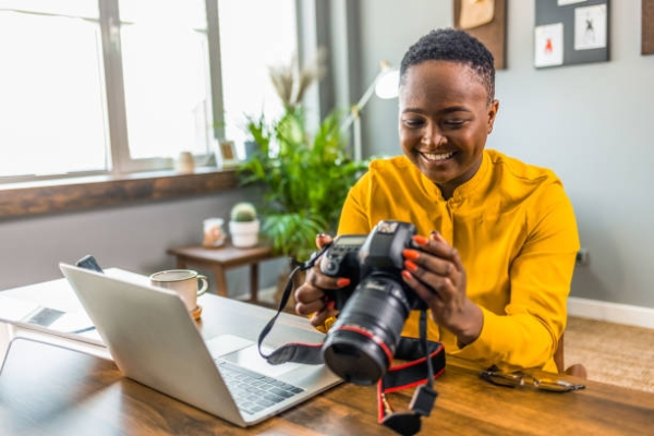 Happy young photographer holding a dslr camera in her home office. Female photographer smiling cheerfully while working at her desk. Creative female freelancer working on a new project.